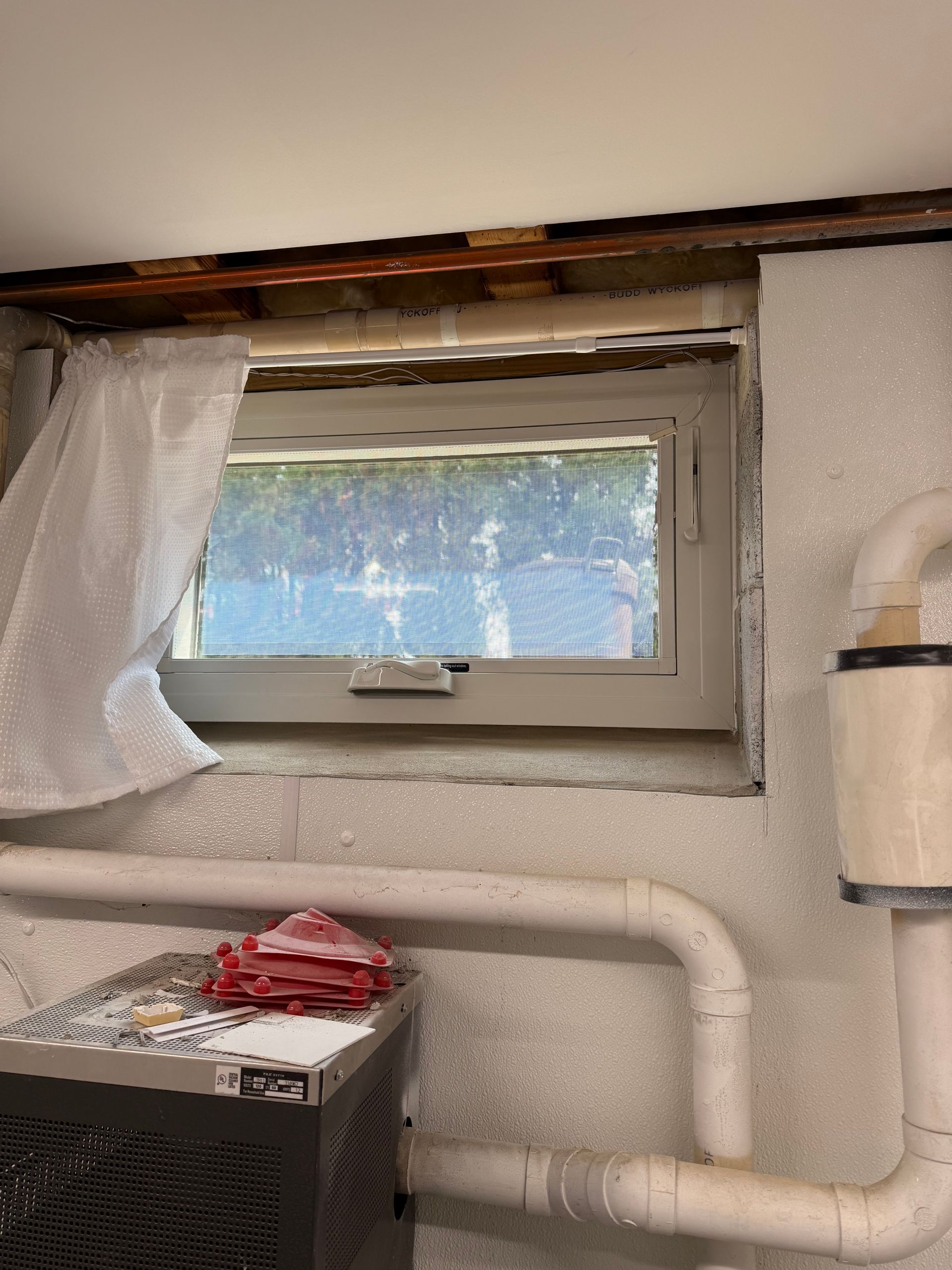 Basement window with a white frame, partially covered by bubble wrap and a screen, on a concrete wall.