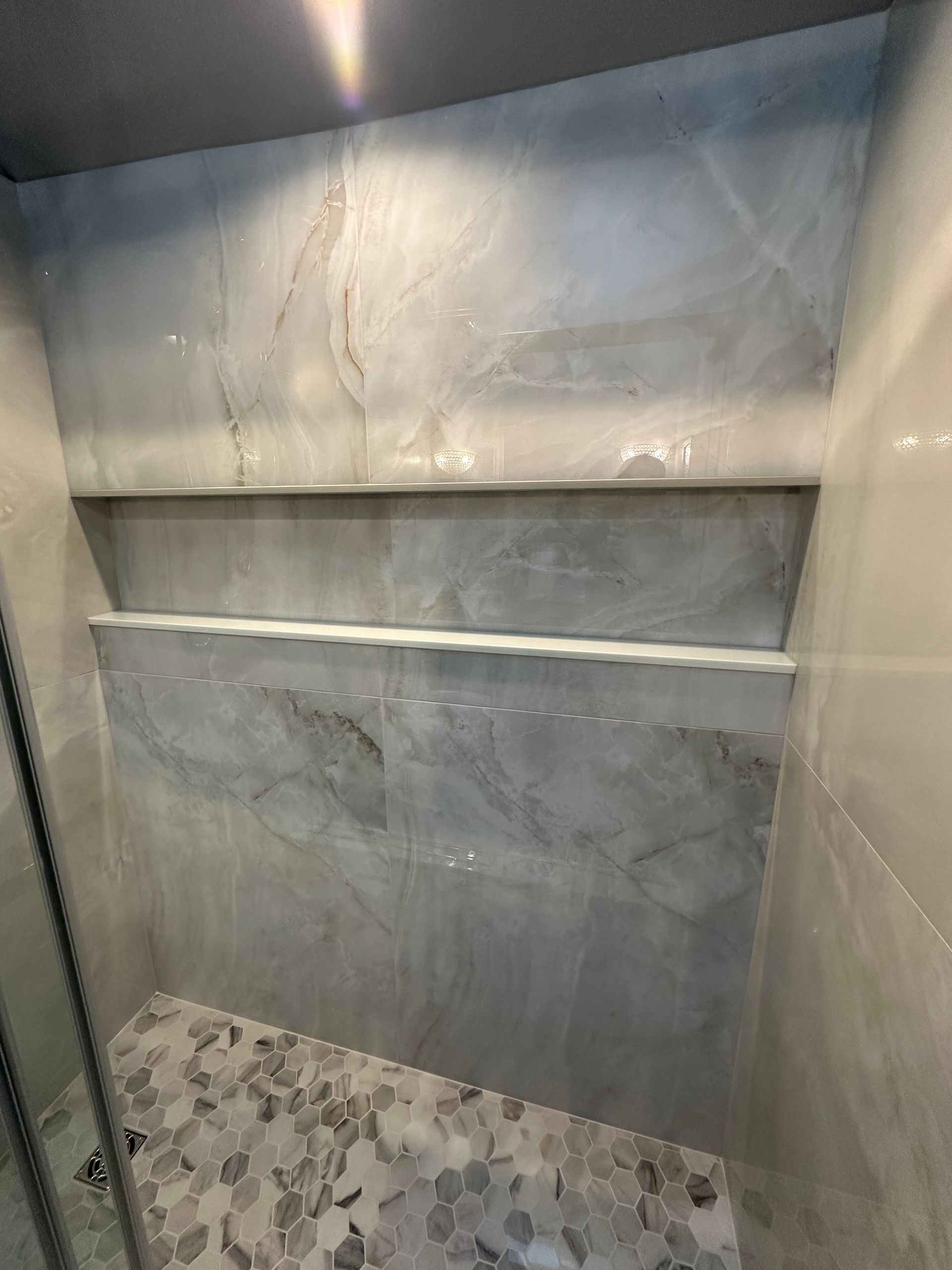 Shower with grey marble tile, built-in shelves, and a pebble floor.