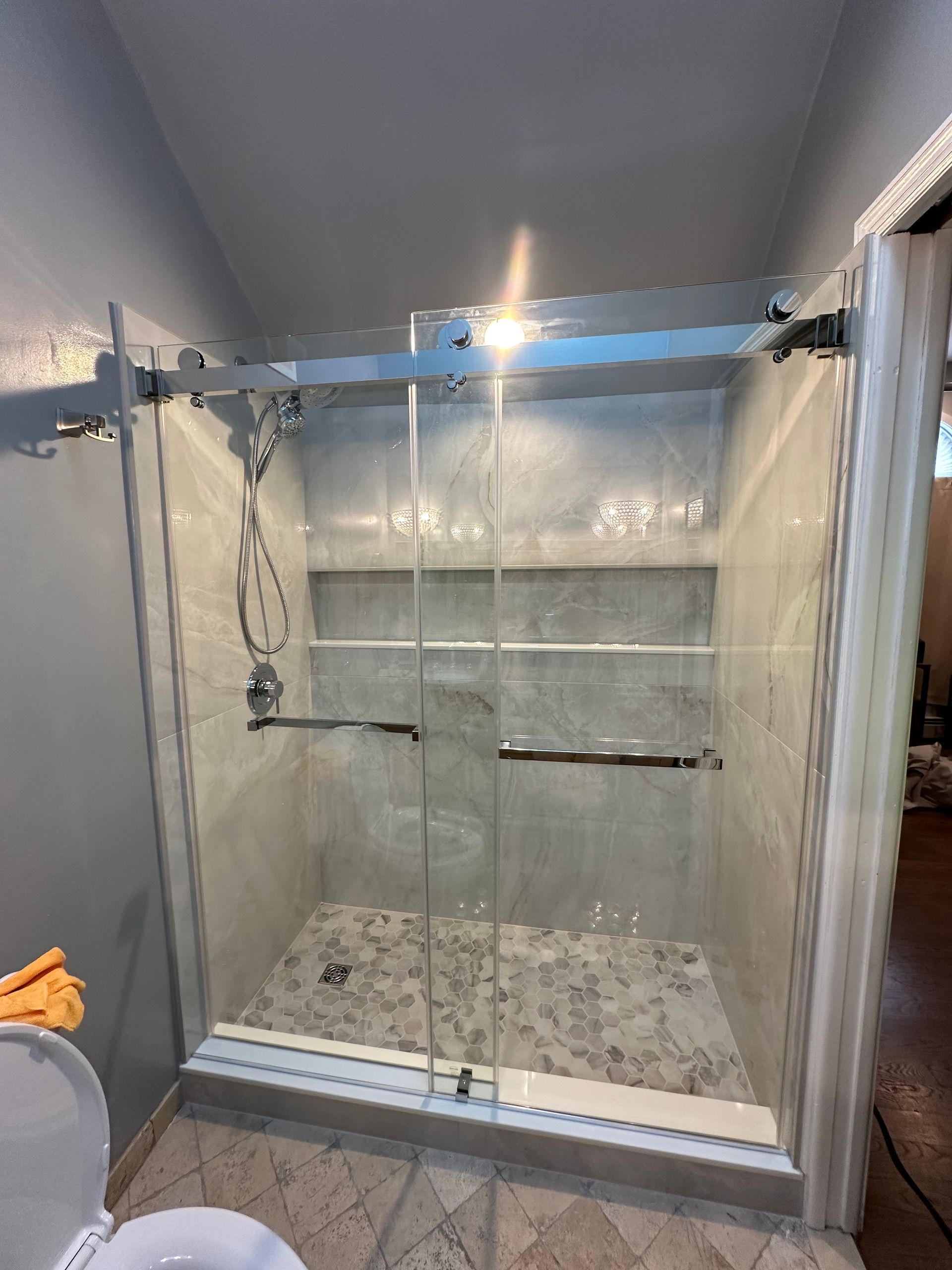 A modern, glass-enclosed shower with gray tiled walls and floor, and silver hardware.