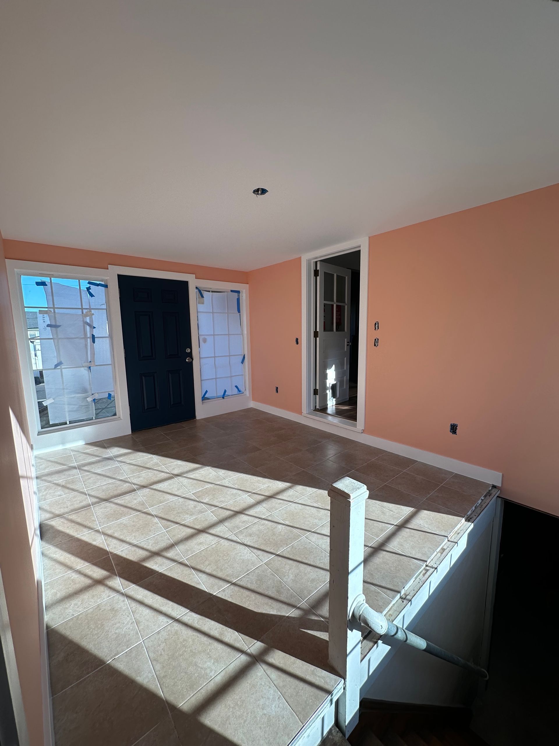 Empty room with peach walls, light wood floors, and white-framed doors. Sunlight streams in.