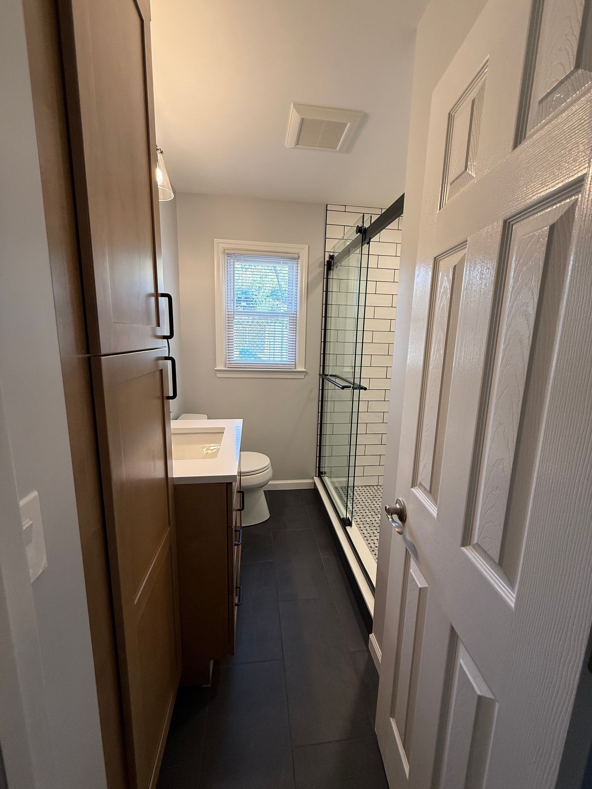 Bathroom with dark floor, shower with black and white tile, wooden vanity, and tall storage cabinet.