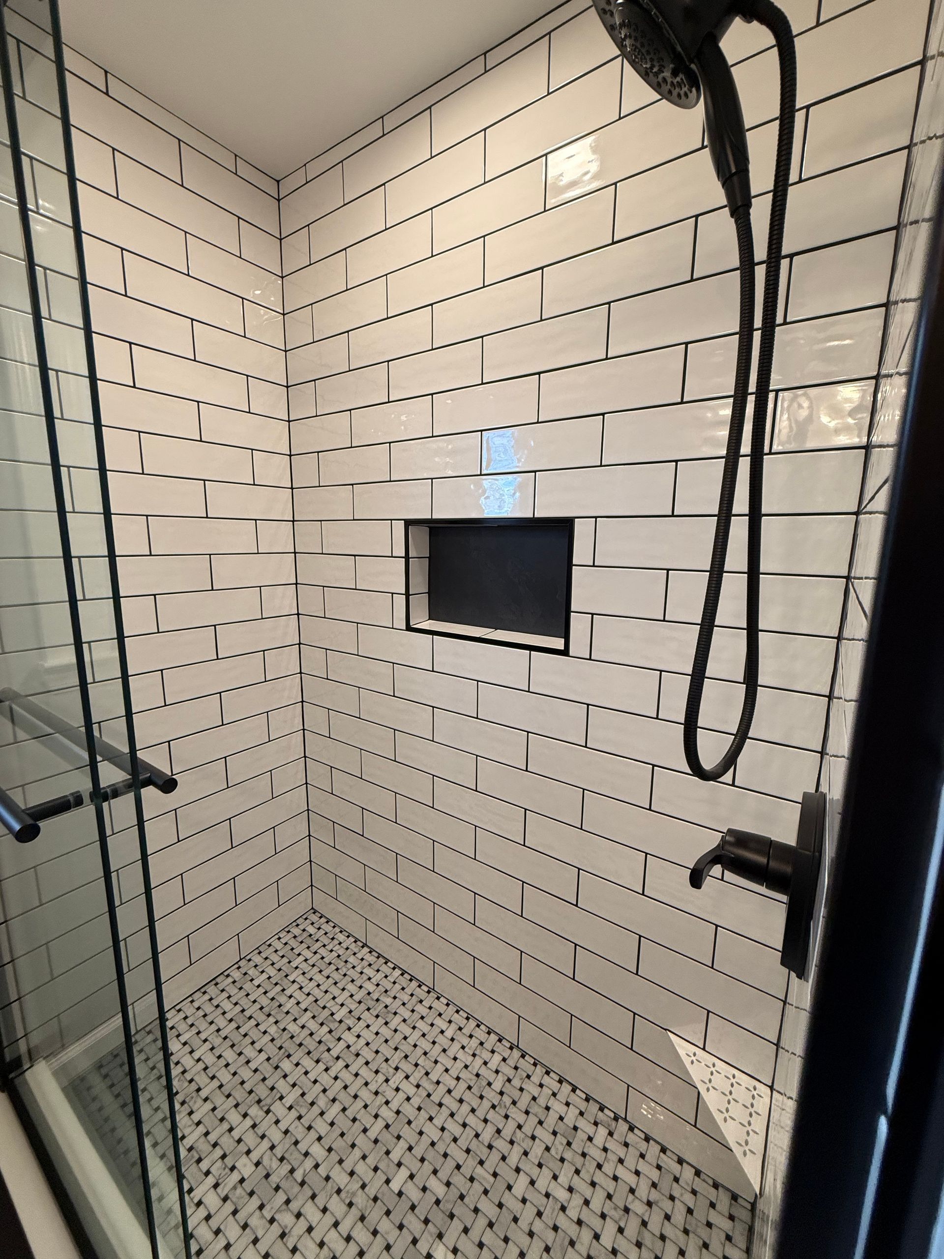White tiled shower with black grout, black fixtures, and glass door.