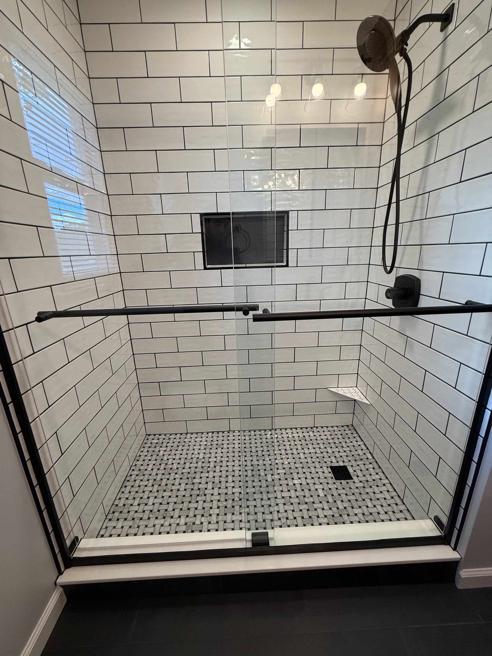 Modern shower with white brick-style tiles, black trim, glass doors, and a dark floor.