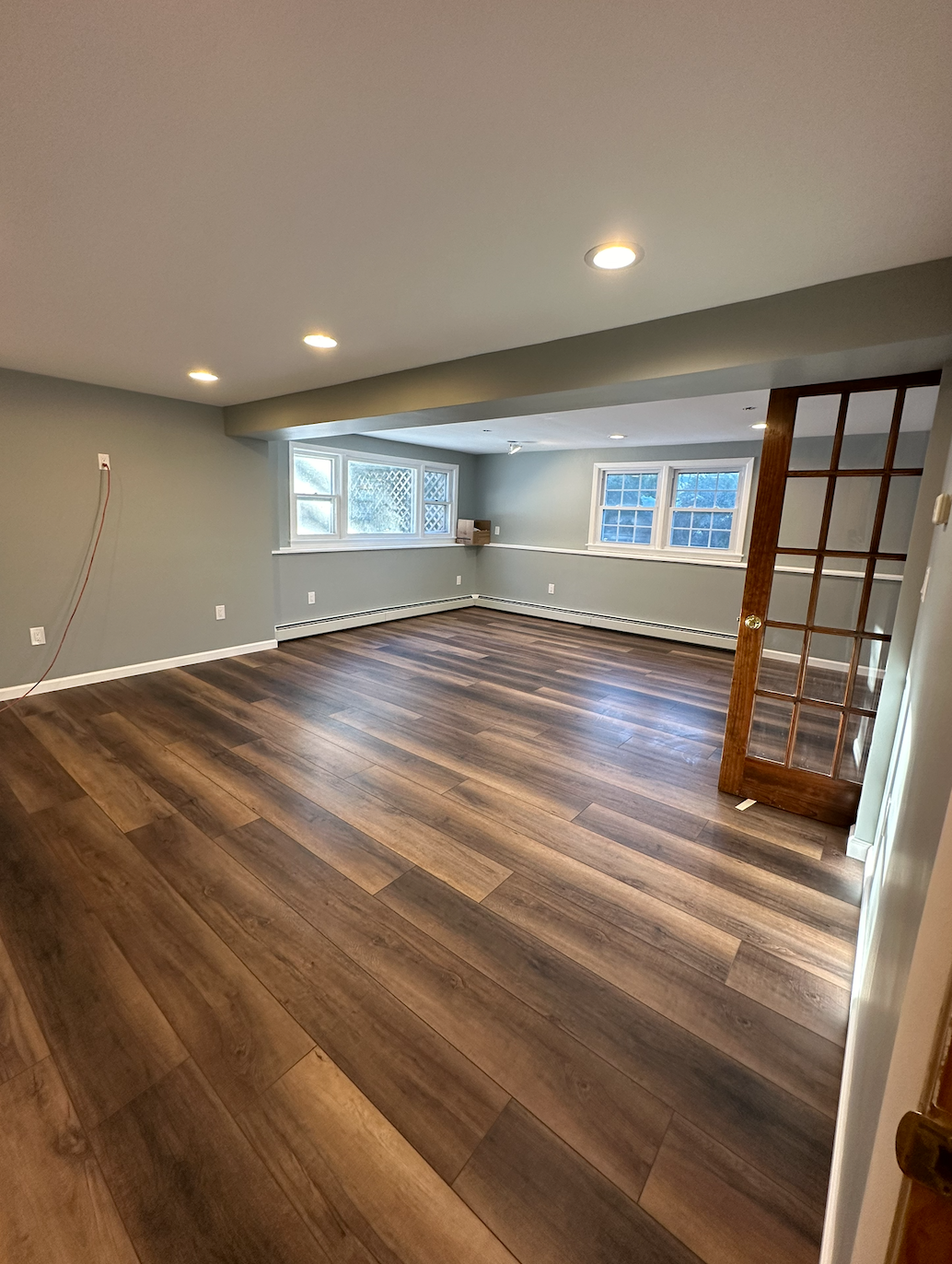 Empty basement room with gray wood-look flooring, white walls, and a ceiling light.
