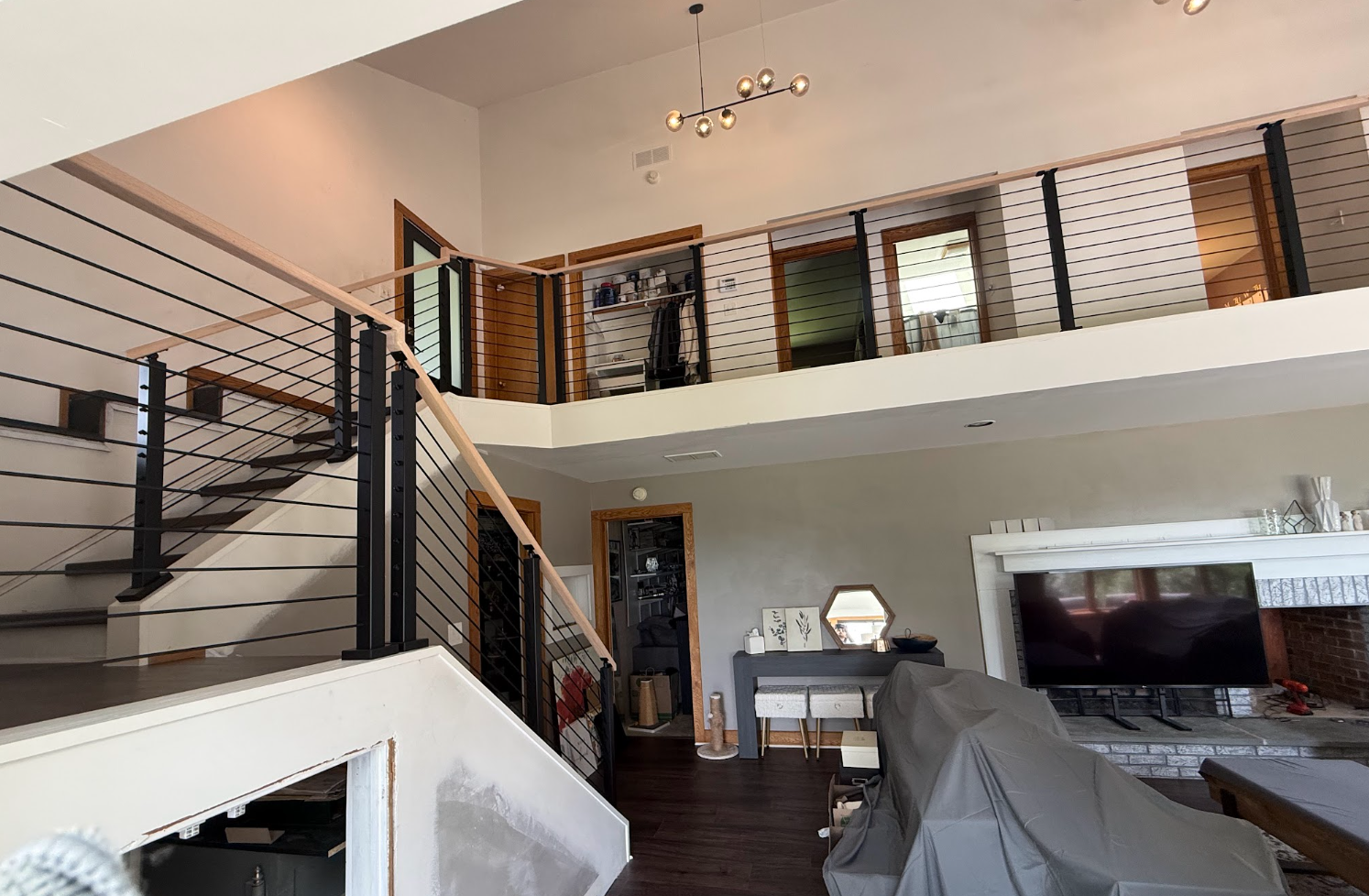 Modern loft living room with staircase, balcony railing, sofa, and fireplace on dark wood floors