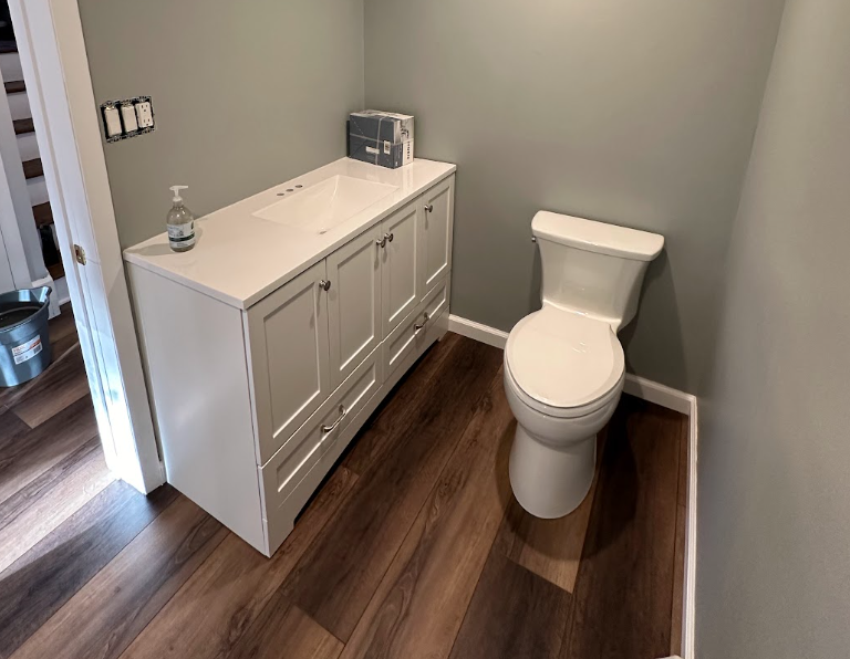 Small bathroom with gray walls, wood floor, white vanity, and toilet.