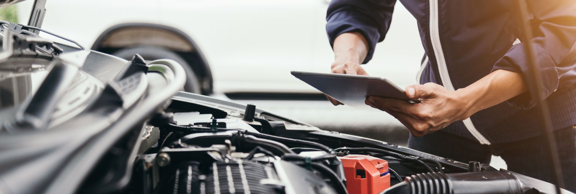 a man is looking under the hood of a car while holding a tablet