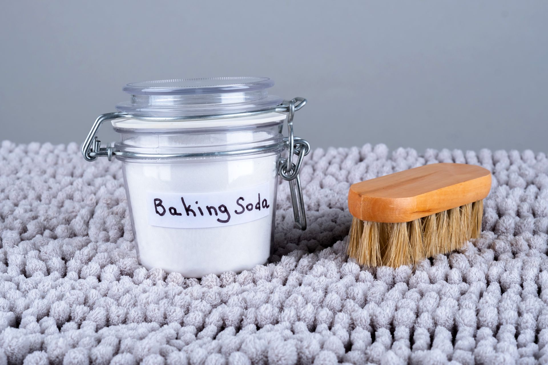 Jar of baking soda and brush on a light gray, textured rug.