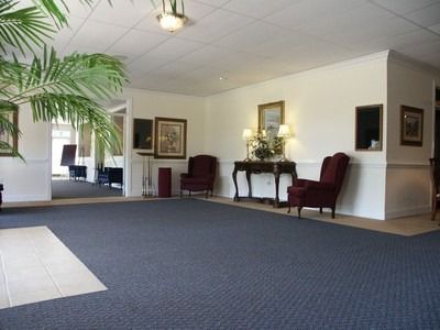 Empty lobby with blue carpet, cream walls, red chairs, and a potted palm near a reception area