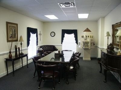 Conference room with dark wood table and chairs, white walls, windows with dark curtains, and decorative cabinets.