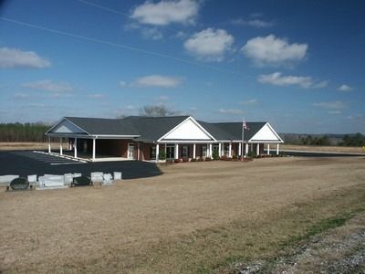 Single-story building with white columns on a wide gravel lot under a blue sky