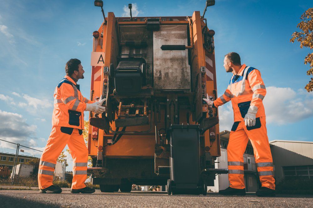 Two Men Are Standing Next To A Garbage Truck — Hastings Diesel Service In Wauchope, NSW