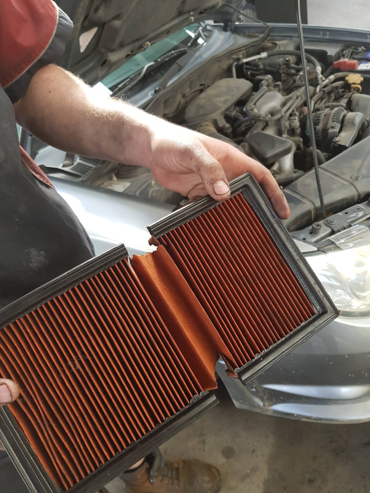 A Man Is Holding Two Air Filters In Front Of A Car With The Hood Open — Hastings Diesel Service In Wauchope, NSW