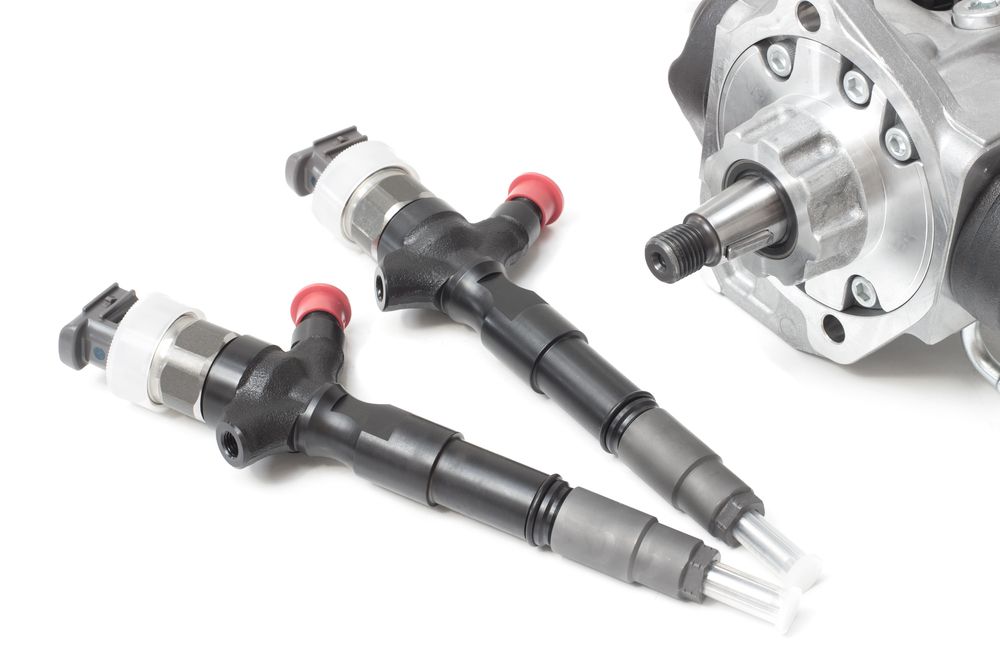 Two Fuel Injectors Are Sitting Next To A Fuel Pump On A White Surface — Hastings Diesel Service In Wauchope, NSW
