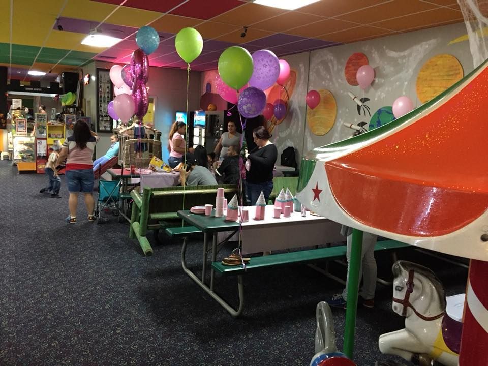 A group of people are gathered in a room with balloons and a merry go round