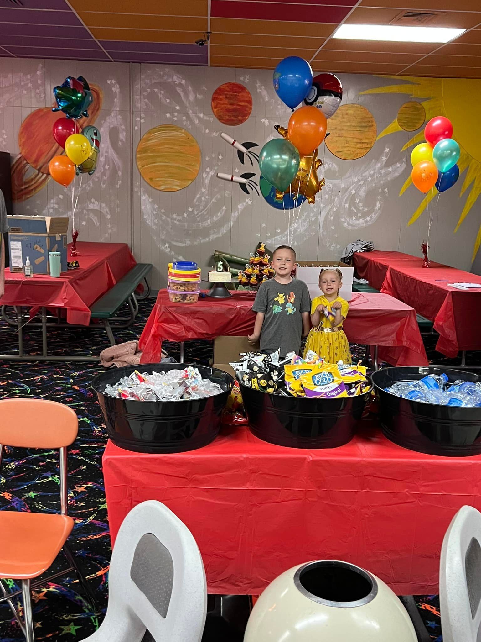 A boy and a girl are standing in front of a table with balloons on it.