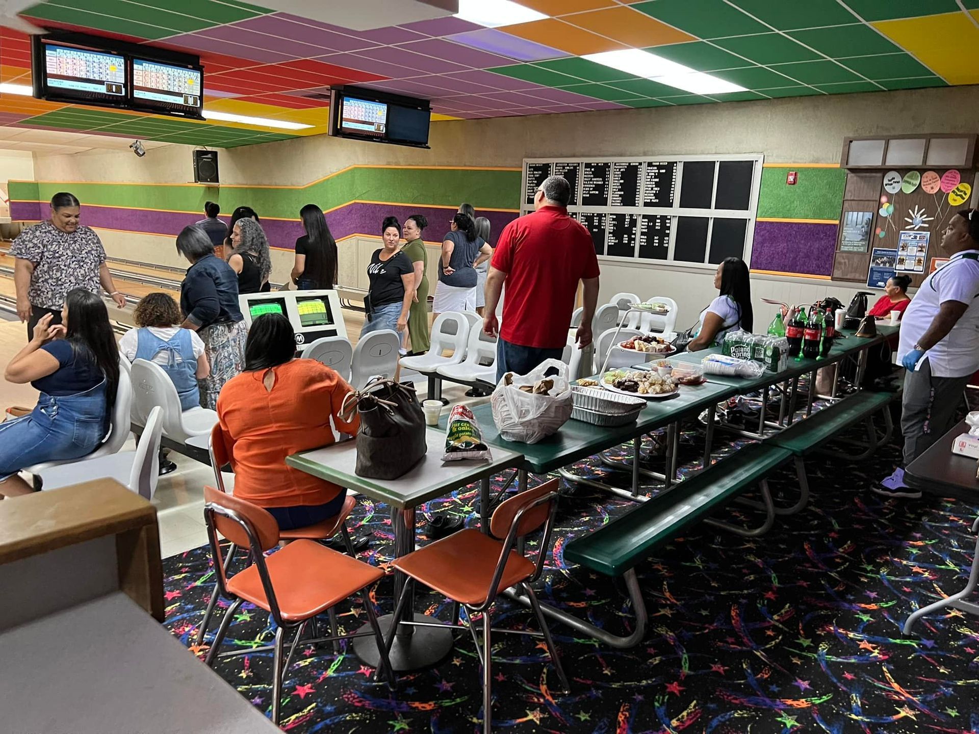 A group of people are sitting at tables in a bowling alley.