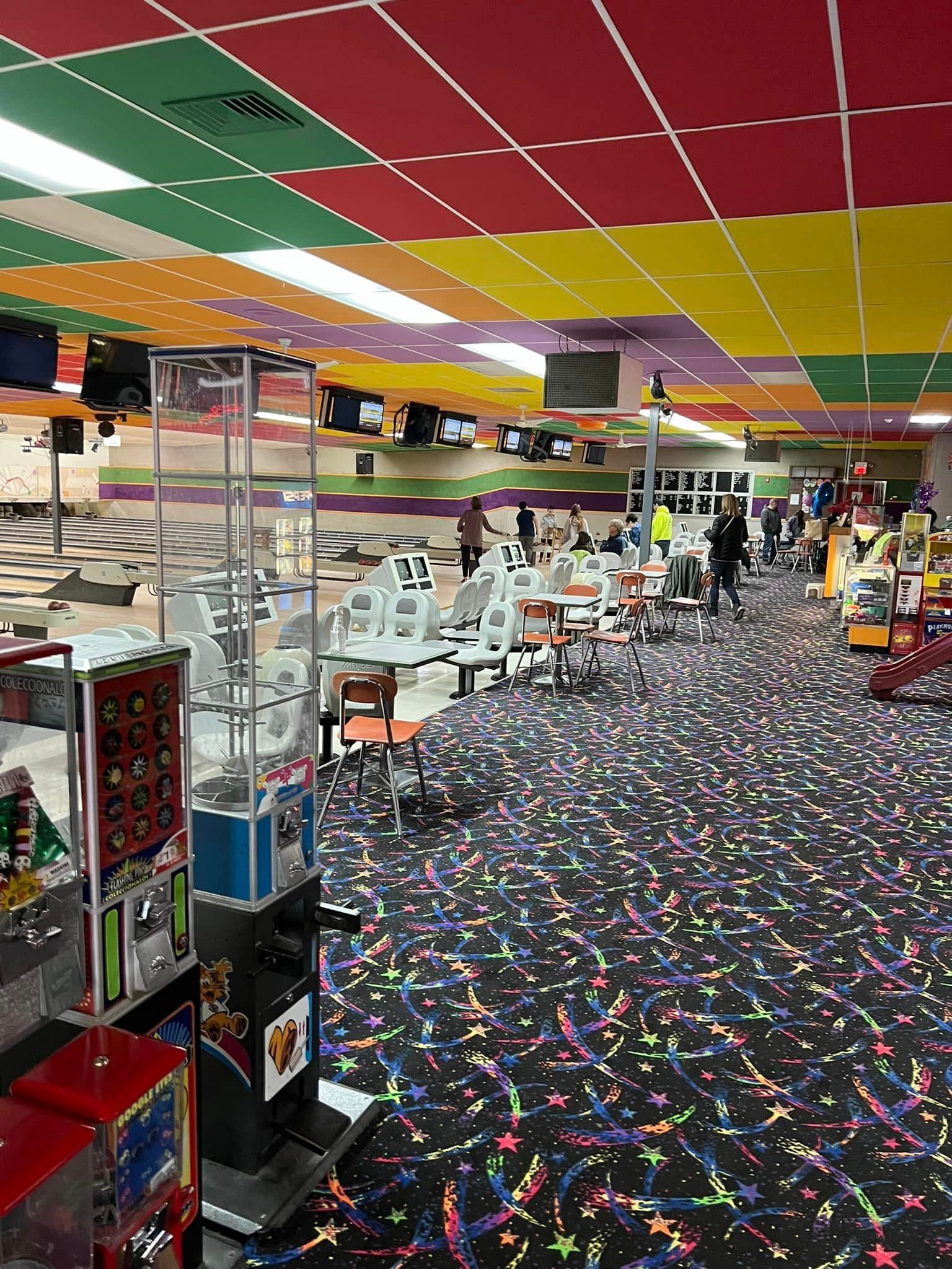 A bowling alley with tables and chairs and a colorful ceiling.