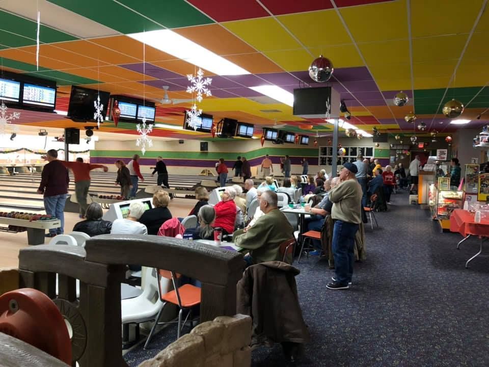 A group of people are sitting at tables in a bowling alley.
