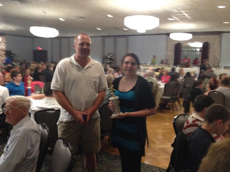 A man and a woman are standing in a crowded room holding a trophy