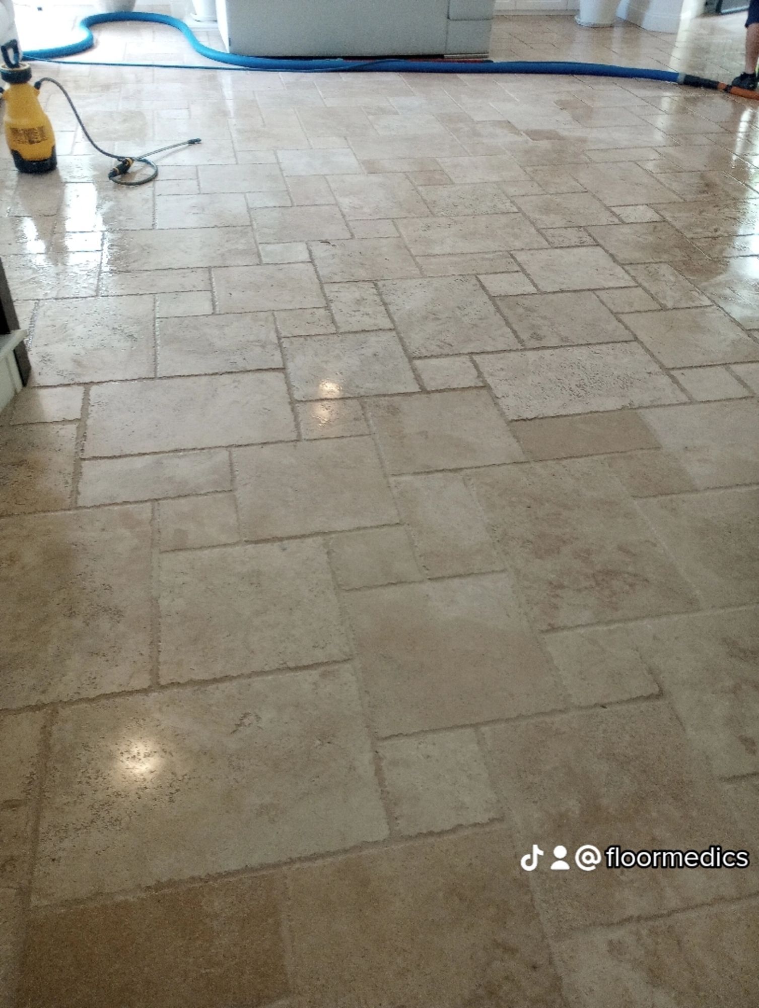 A person is cleaning a tile floor with a vacuum cleaner.