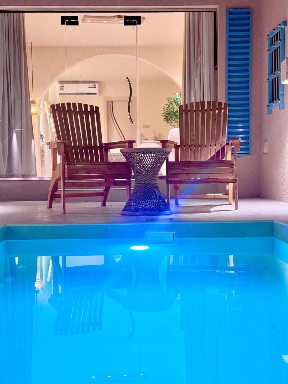 Two wooden chairs and table on patio, facing a pool with blue water.
