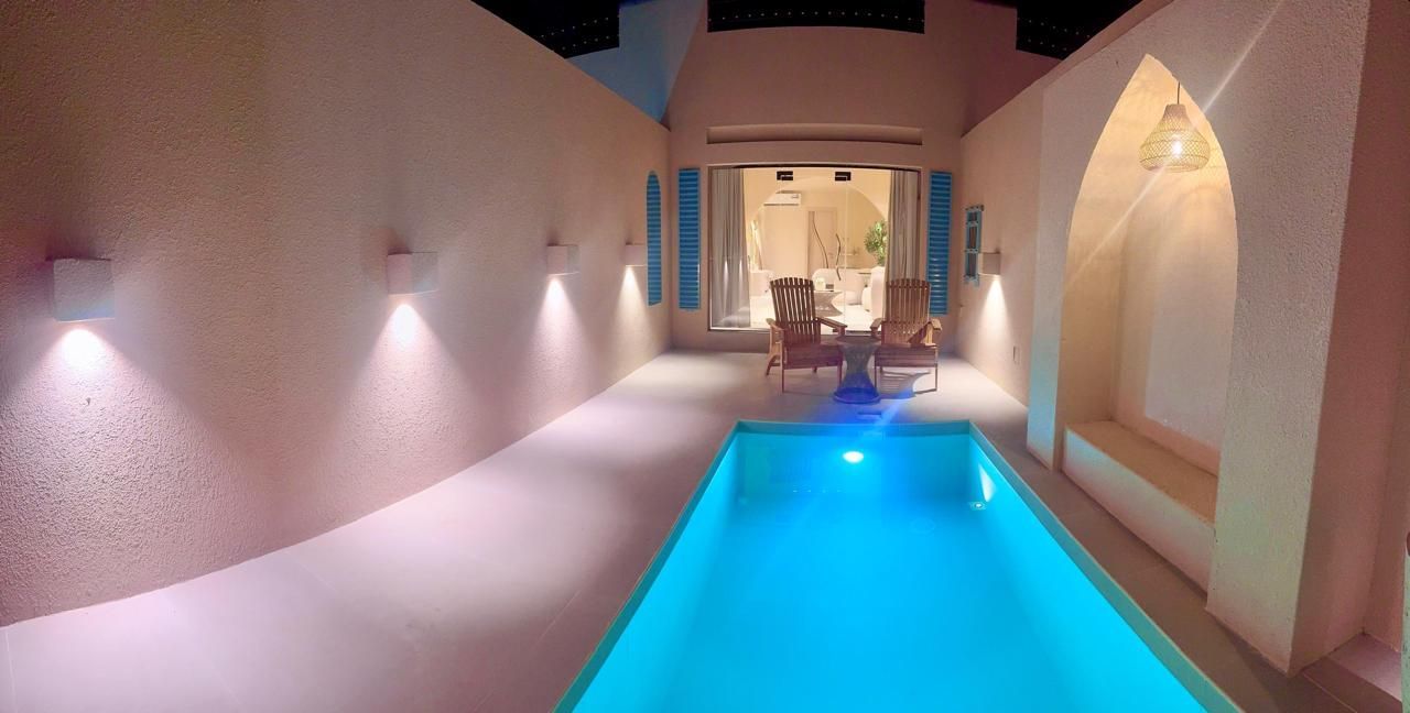 Small outdoor pool with turquoise water, flanked by illuminated walls.  Seating area visible beyond.