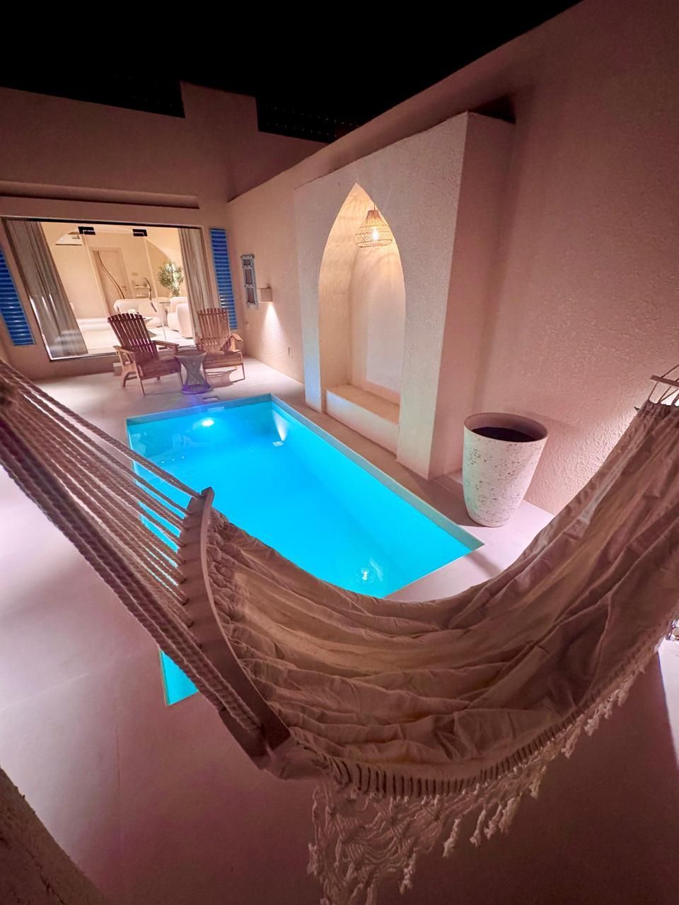 Cozy courtyard with small pool, hammock, and arched wall feature. Bright blue water, white walls.