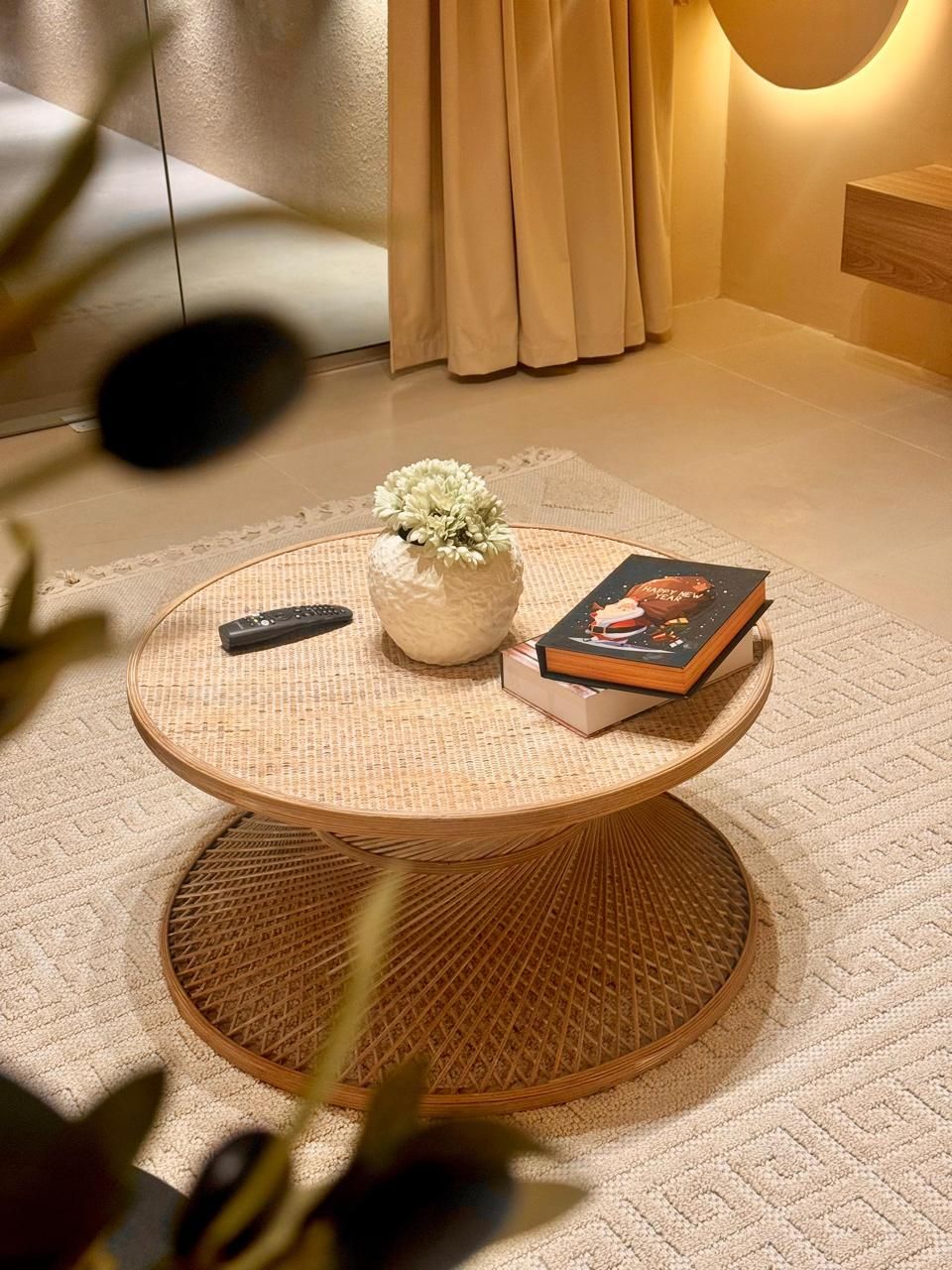 Round rattan coffee table with books, vase, remote, and neutral rug.