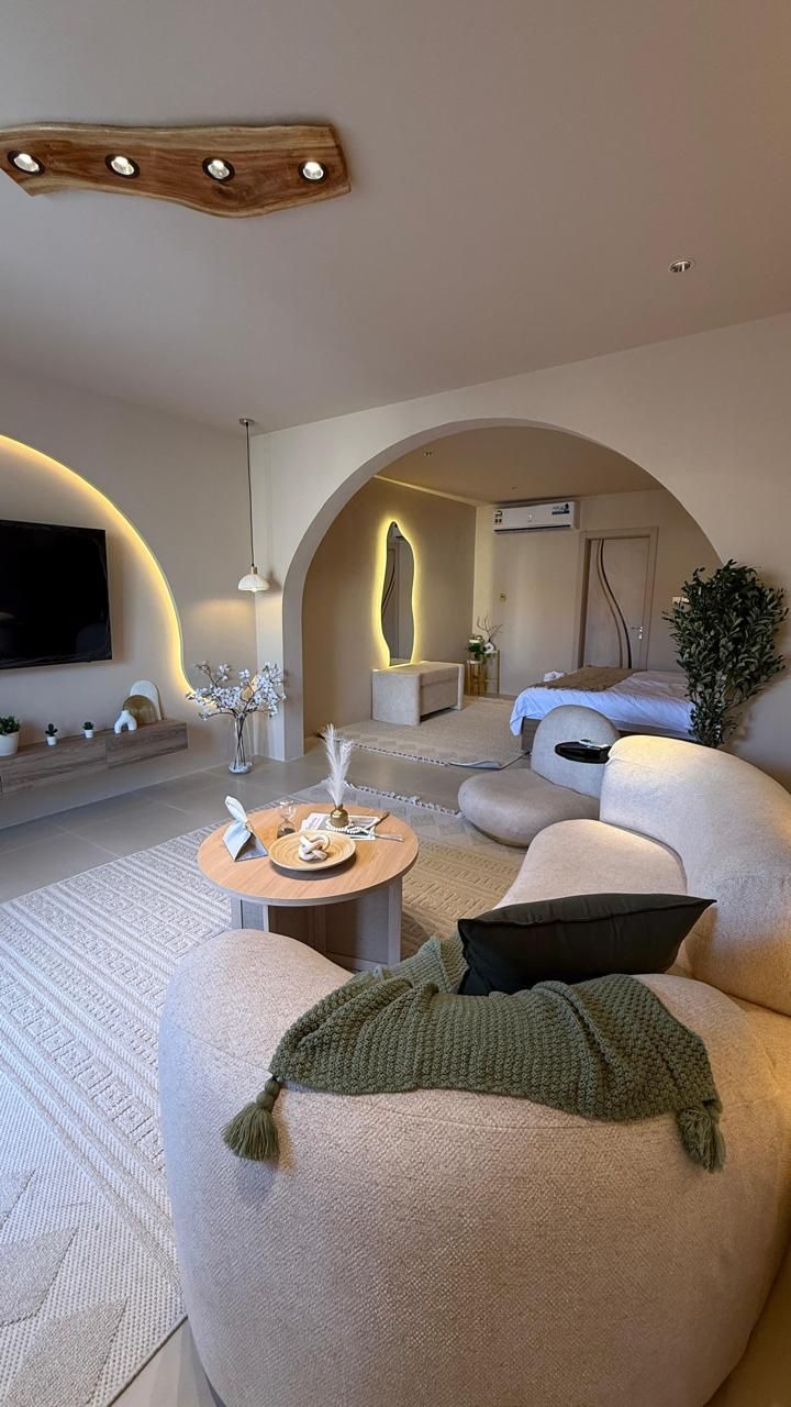Cozy living room with beige furniture, a laptop, and an archway leading to a bedroom.