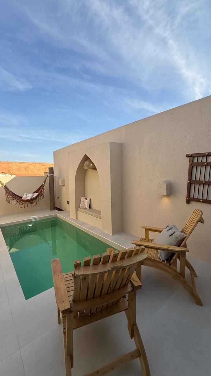 Private pool with lounge chairs, hammock, and beige walls under a blue sky.