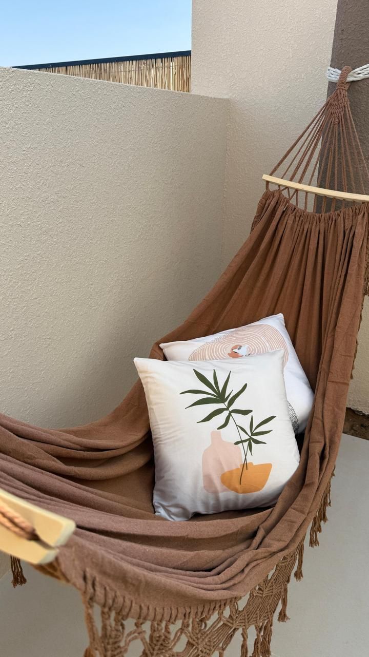 Brown hammock with two pillows against a beige wall, a relaxing outdoor setting.