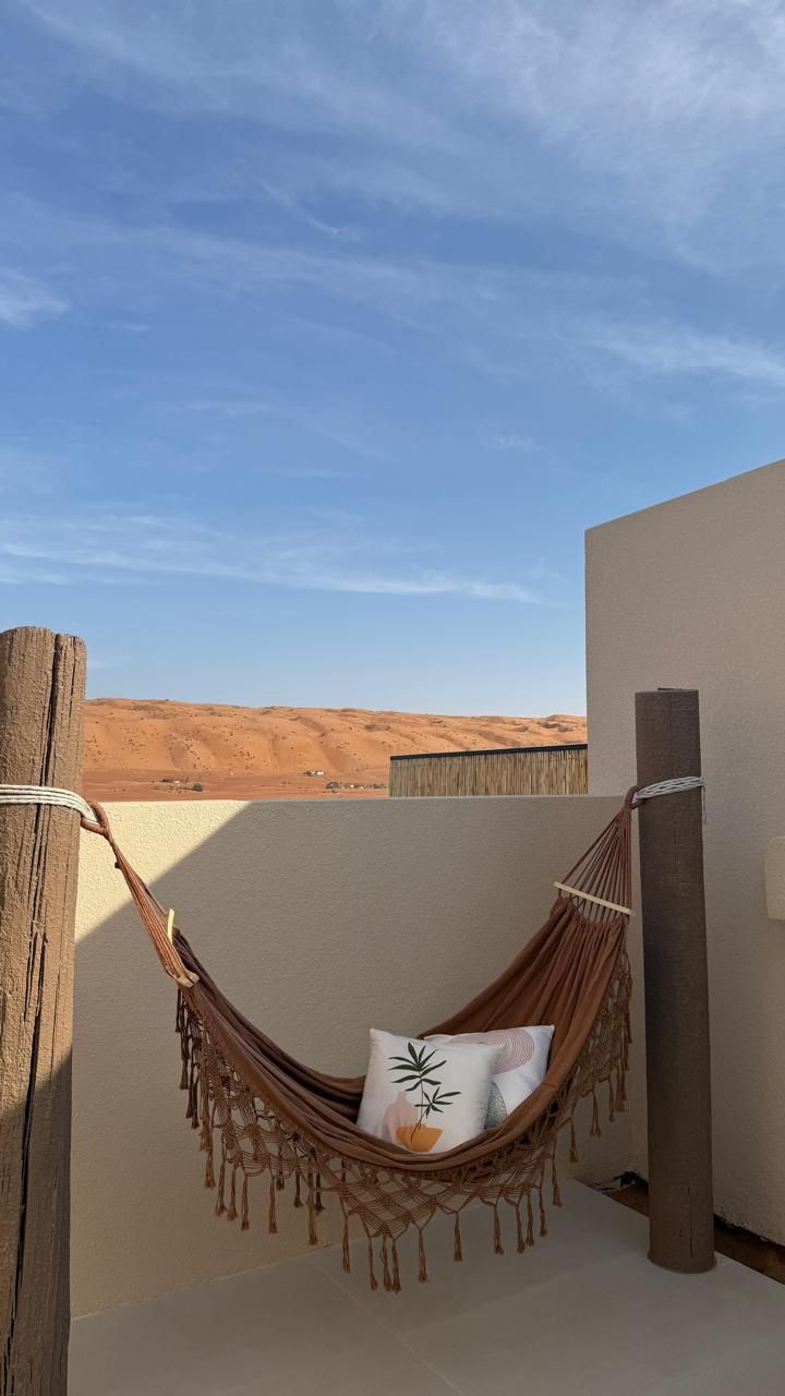 Hammock with pillows on a rooftop, overlooking a desert landscape under a blue sky.