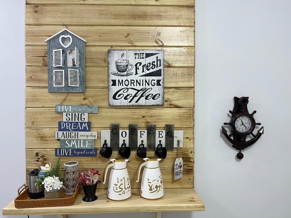 Wooden wall decor with coffee station; signs, mugs, jugs, flowers, and clock.