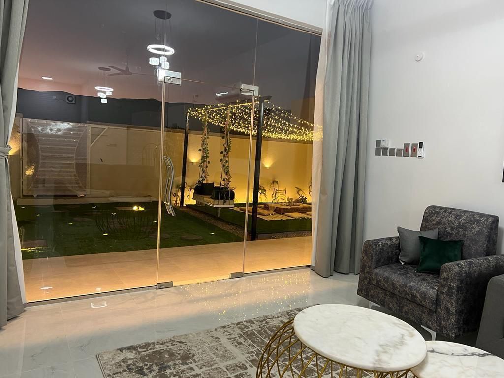 Interior view with glass doors to a lighted yard with swing set, furniture, and marble-topped coffee table.