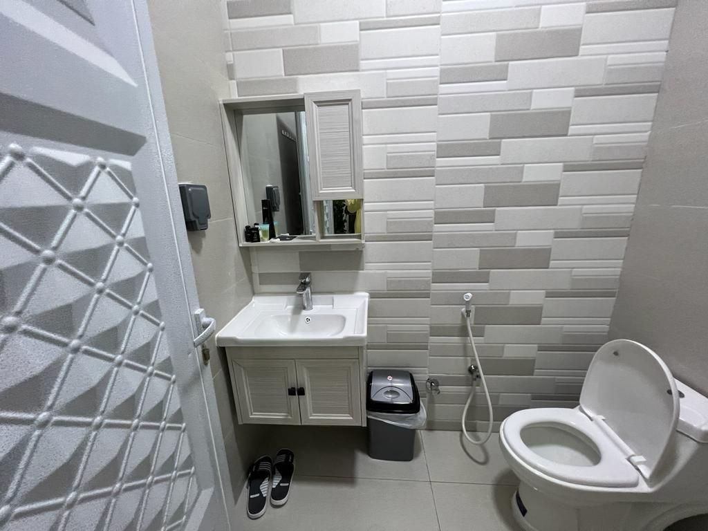 Bathroom with white sink, toilet, and tiled wall. A door is on the left.