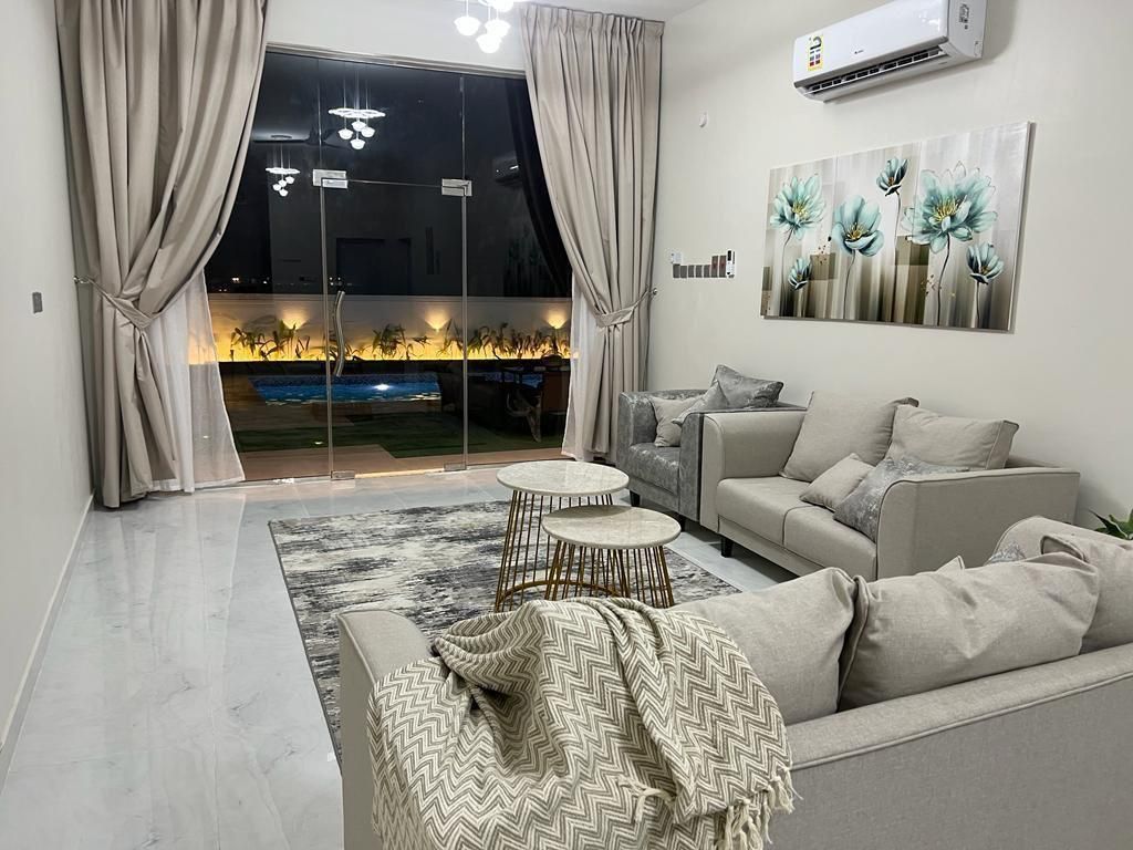 Living room with beige couches, rug, and artwork, with a view of a pool.