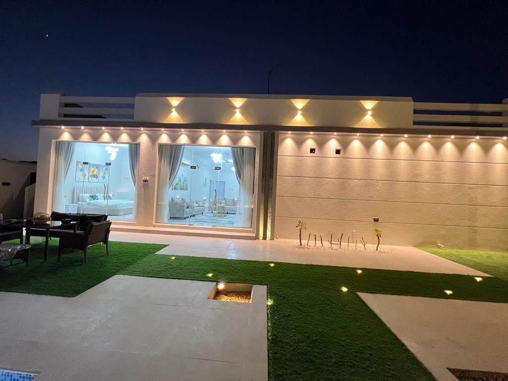 Exterior nighttime view of a modern building with warm lighting, a grassy yard, and an illuminated interior.