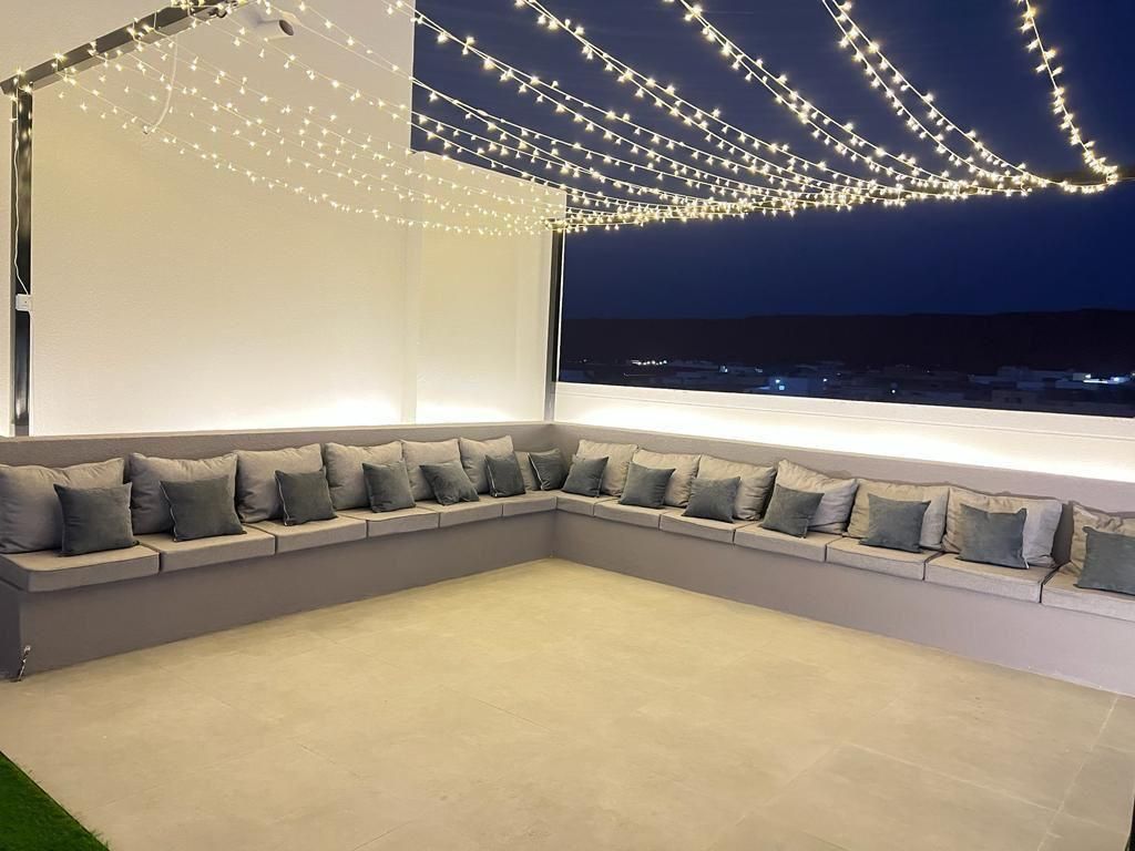 Outdoor lounge area at night with string lights, grey cushions, and ocean view.
