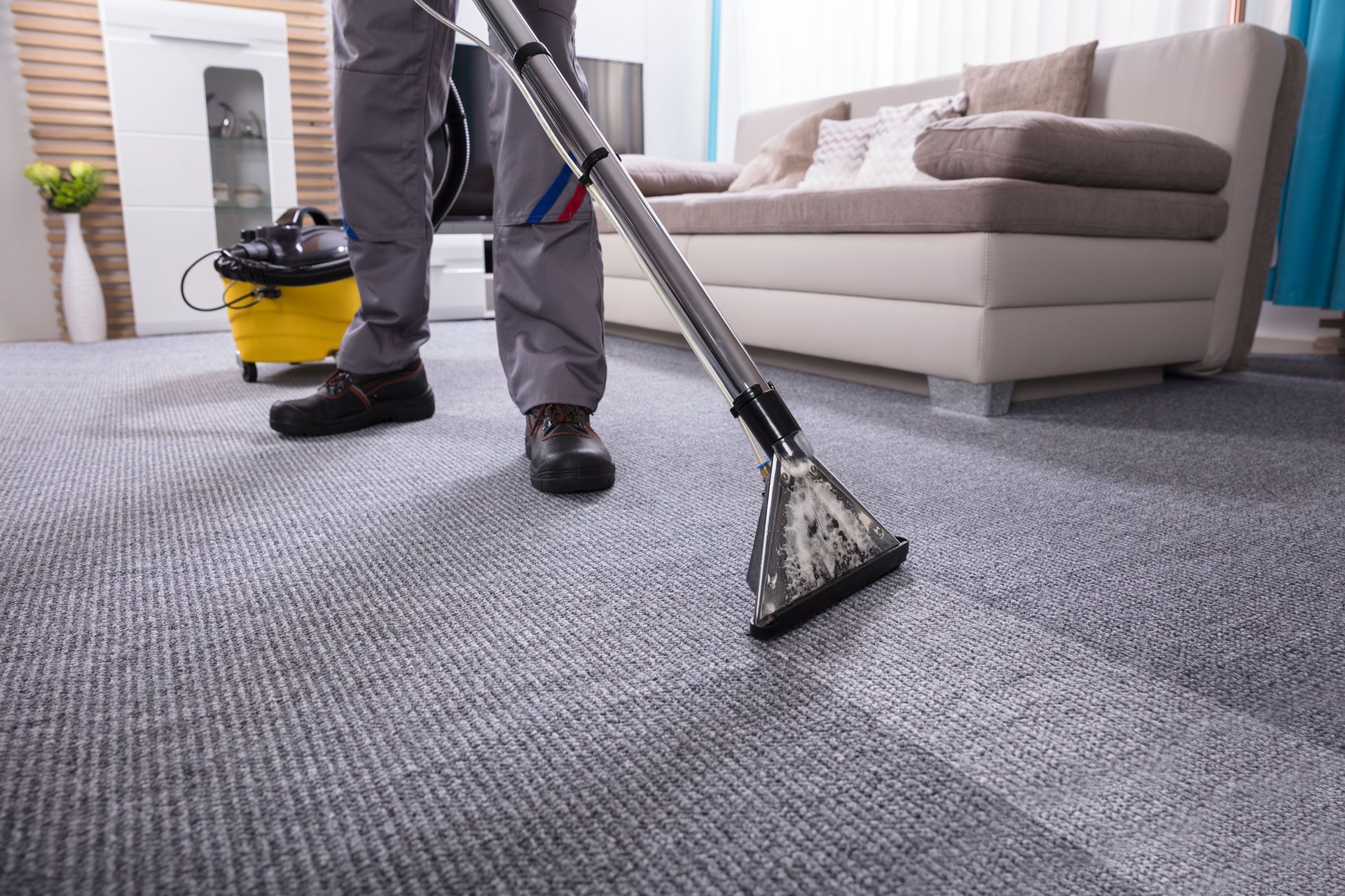 A man is cleaning a carpet with a vacuum cleaner in a living room.