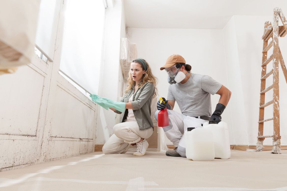 A man and a woman are cleaning a window in a room.