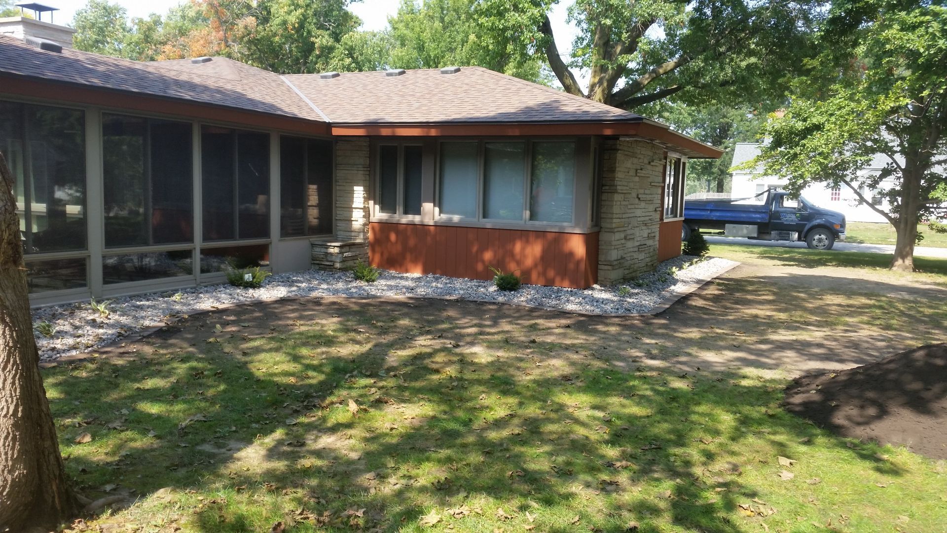 A ranch-style house with a screened porch and stone siding, featuring a rock landscape border and a green lawn.