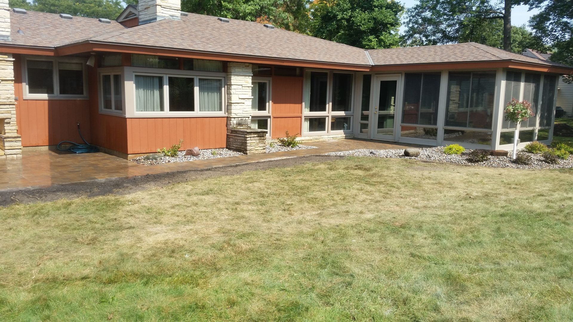 A single-story house with a brown roof, orange siding, stone accents, and a screen porch overlooking a lawn.