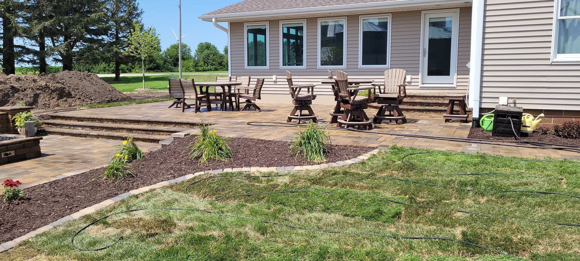 A patio with outdoor furniture and a stone pathway leading to a house with light siding, surrounded by a lawn and mulch.