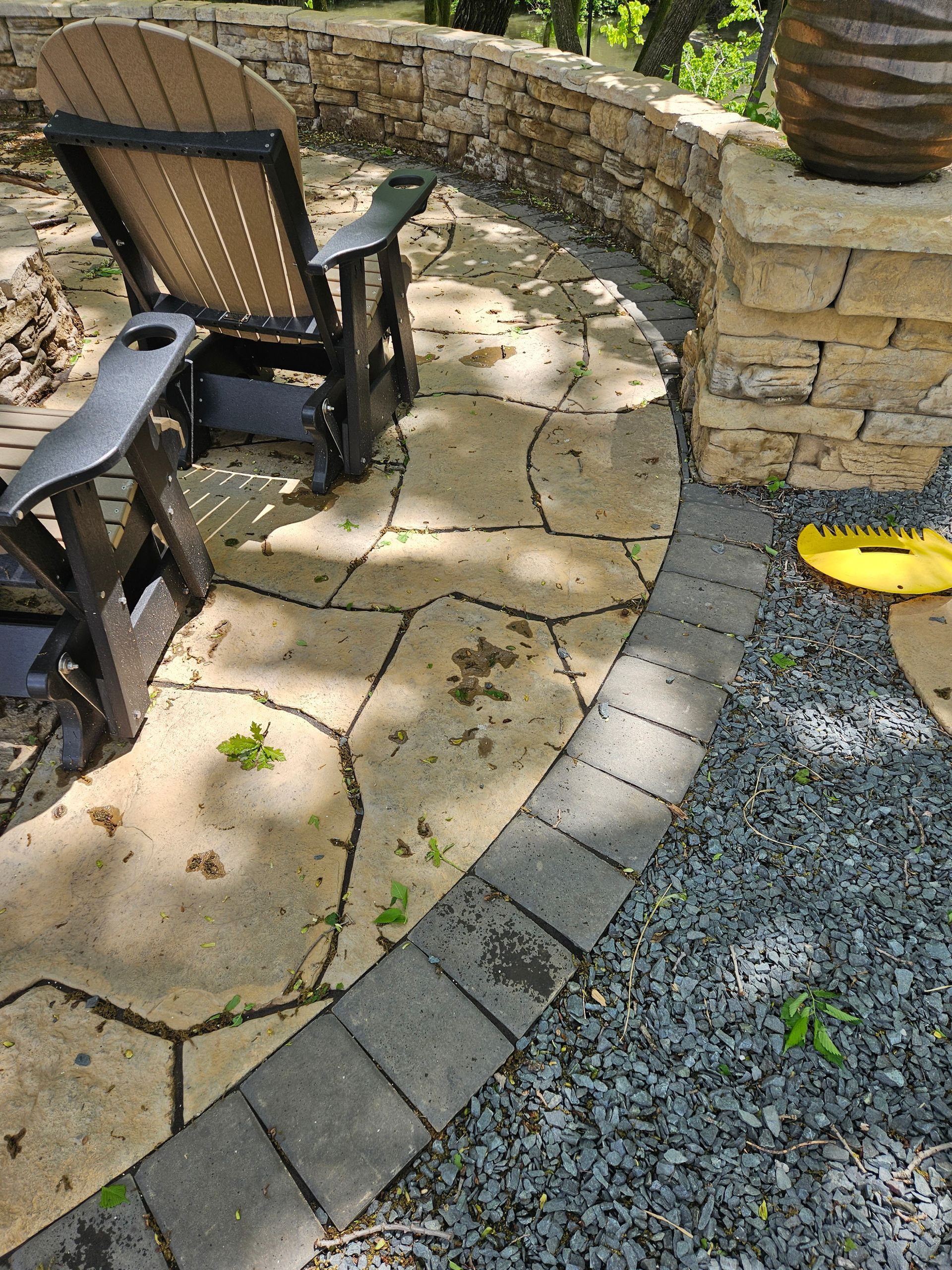 A patio featuring flagstone paving bordered by dark stone bricks, a dark Adirondack chair, and a stone retaining wall.