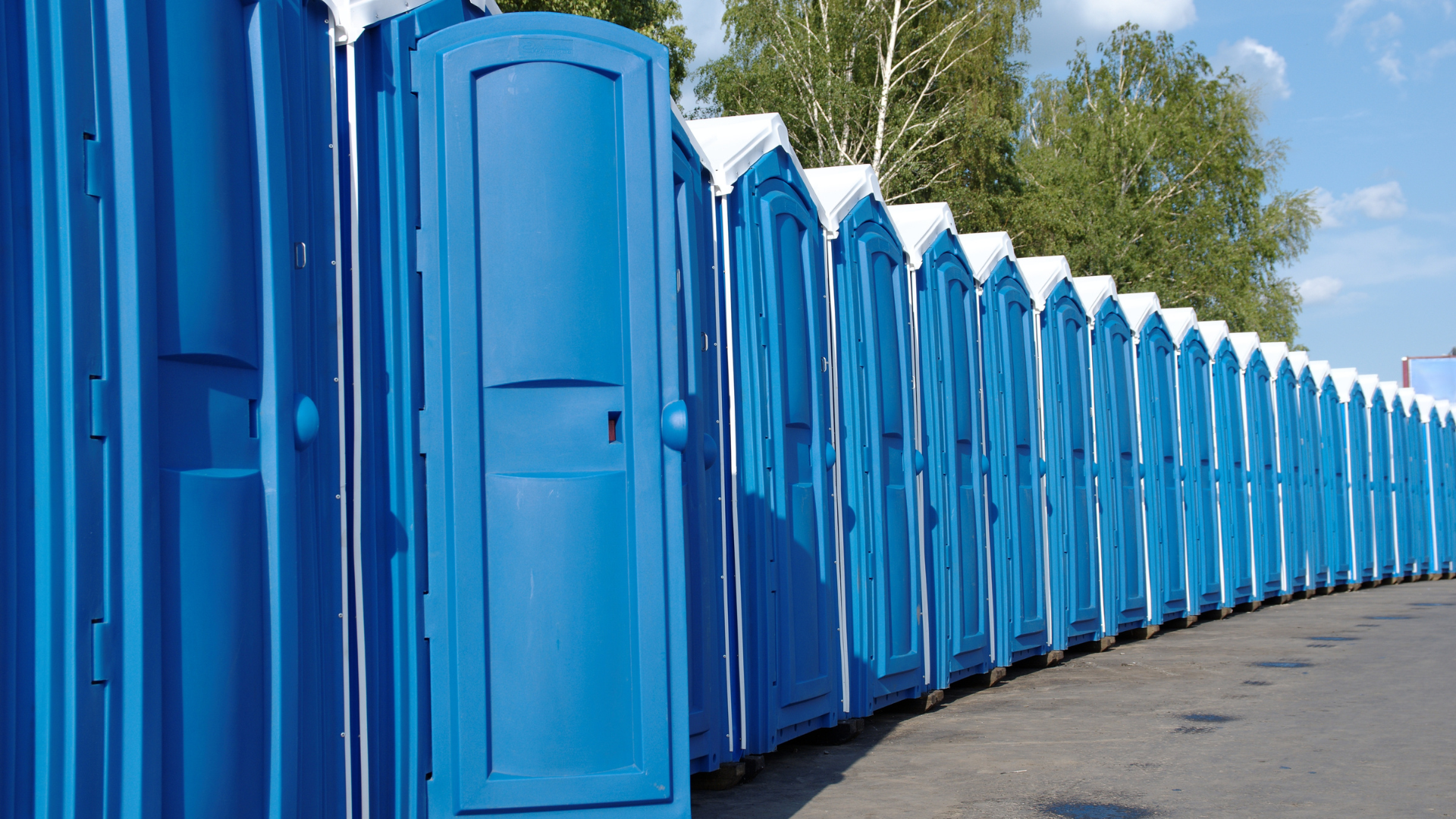 Row of blue portable toilets lined up along a paved road outdoors