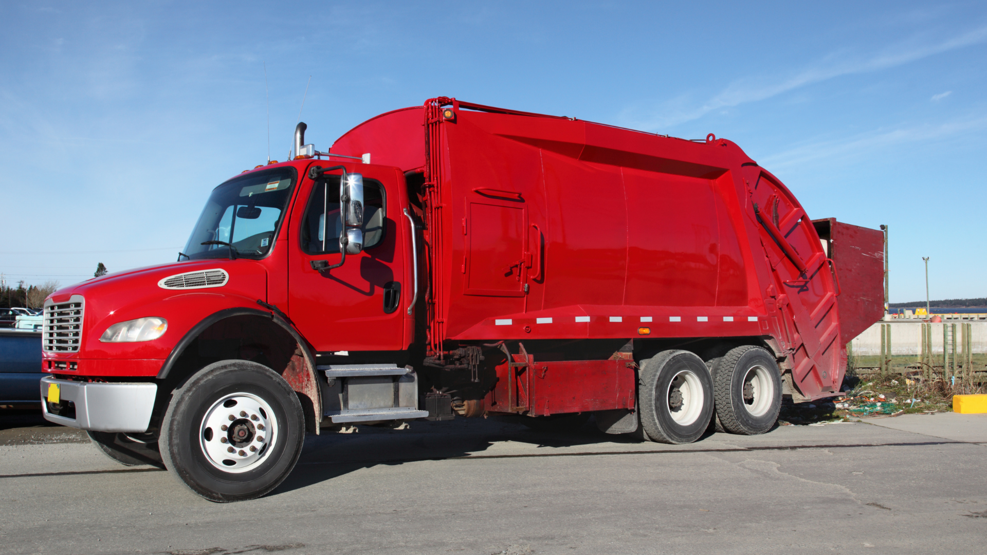Red garbage truck parked under a blue sky.