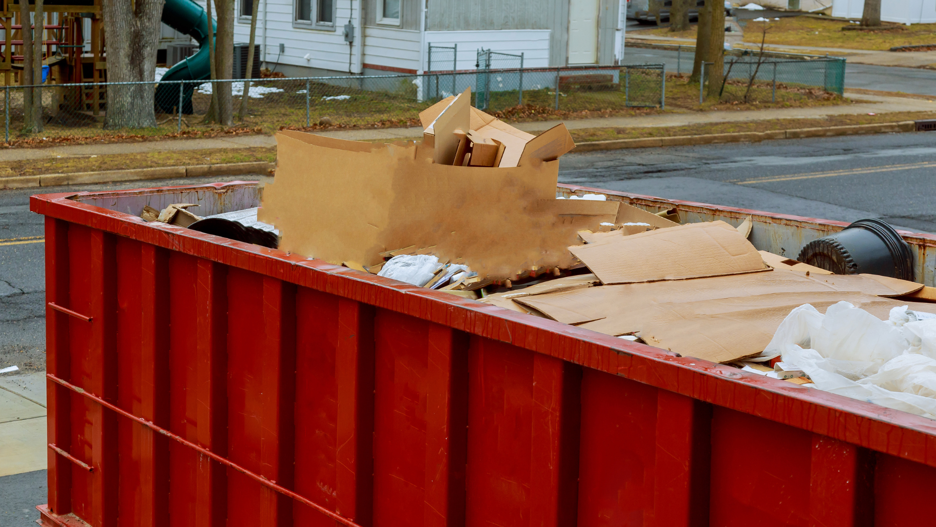 Red dumpster overflowing with cardboard boxes and trash, outdoors.