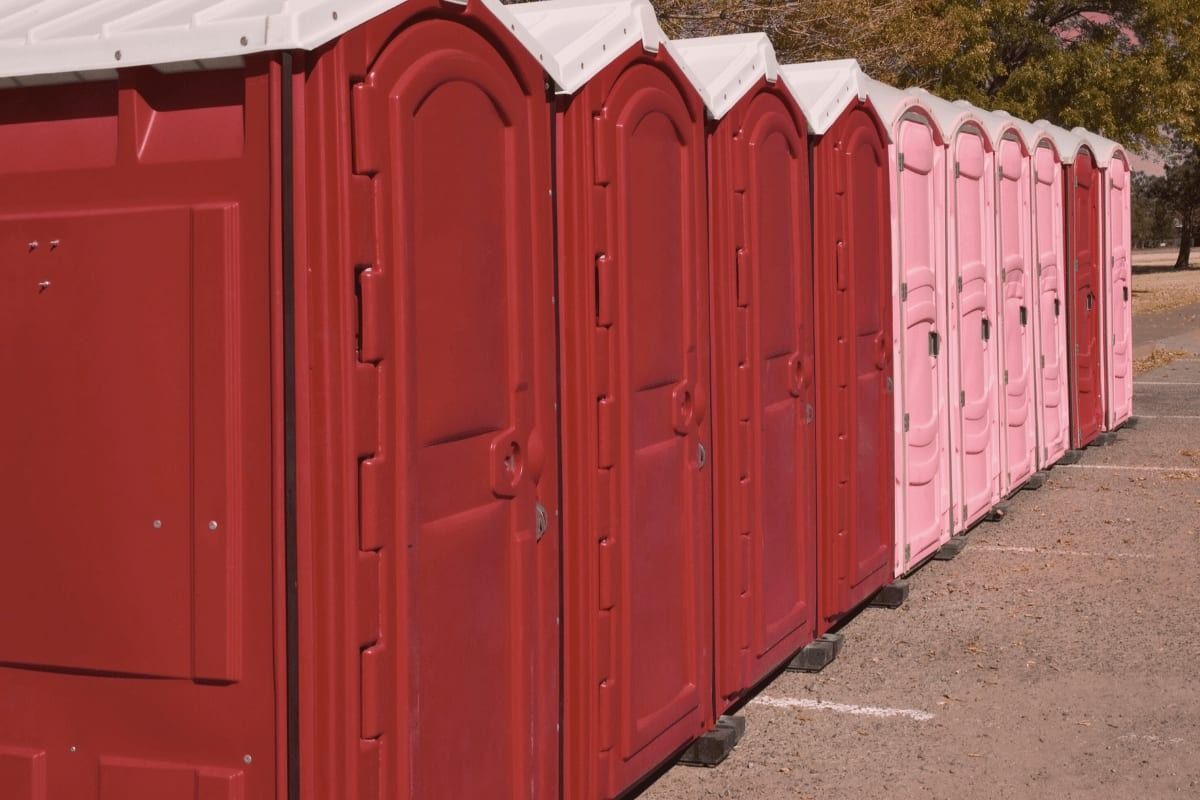 Red and pink portable toilets lined up outdoors.