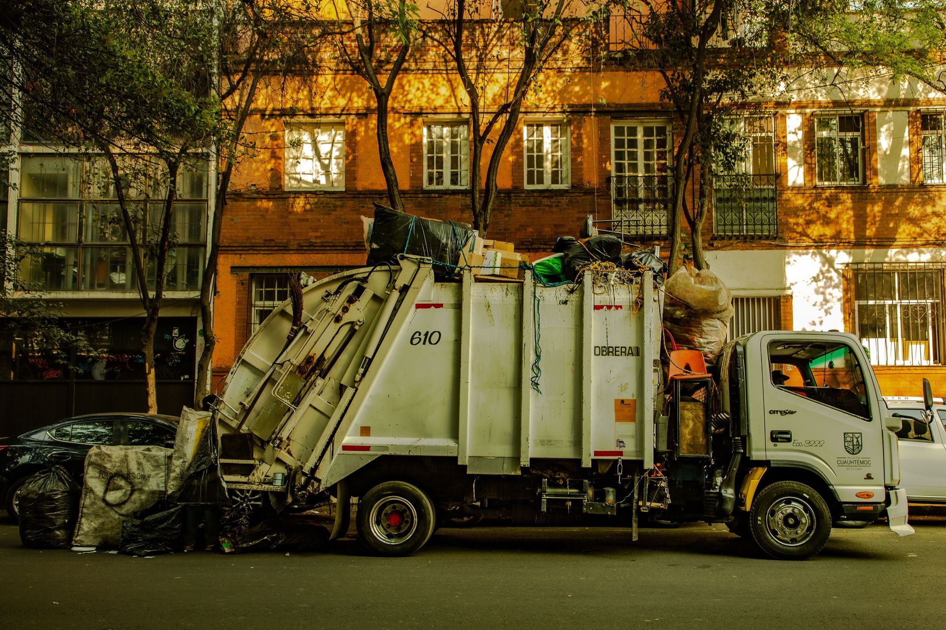 Garbage truck on a city street with apartment buildings and trees in the background